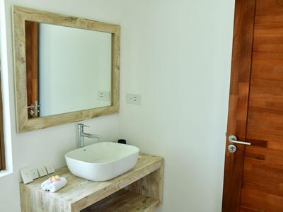 Bagno luminoso con specchio rettangolare, lavabo rotondo bianco e porta in legno.