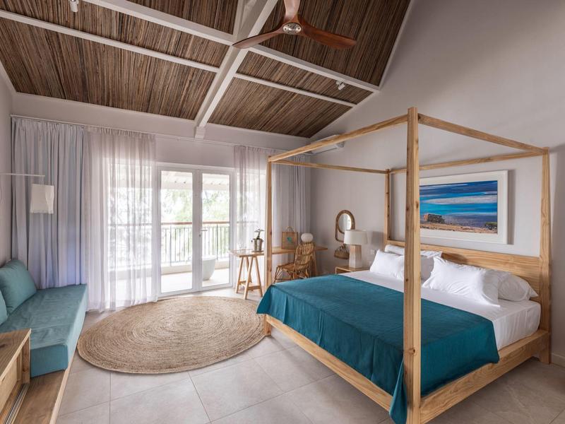 Chambre moderne avec plafond à poutres en bois, lit à baldaquin et couverture turquoise.