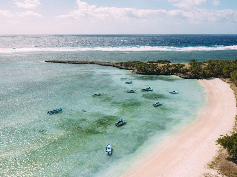 Vue aérienne d'une plage avec eau claire, bateaux et terrain verdoyant.