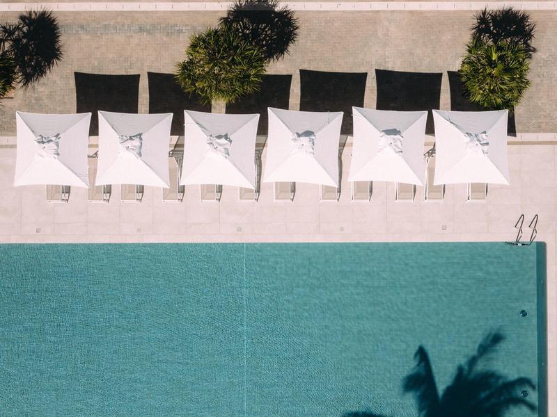 Six parasols blancs avec chaises longues à côté d'une piscine turquoise sur une terrasse.