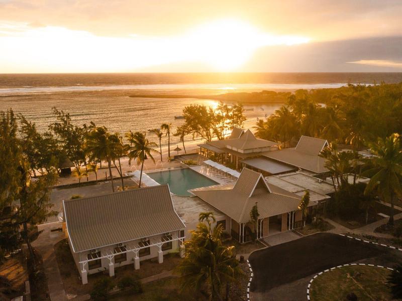 Complexe hôtelier avec piscine en bord de mer au coucher du soleil, ambiance paisible.