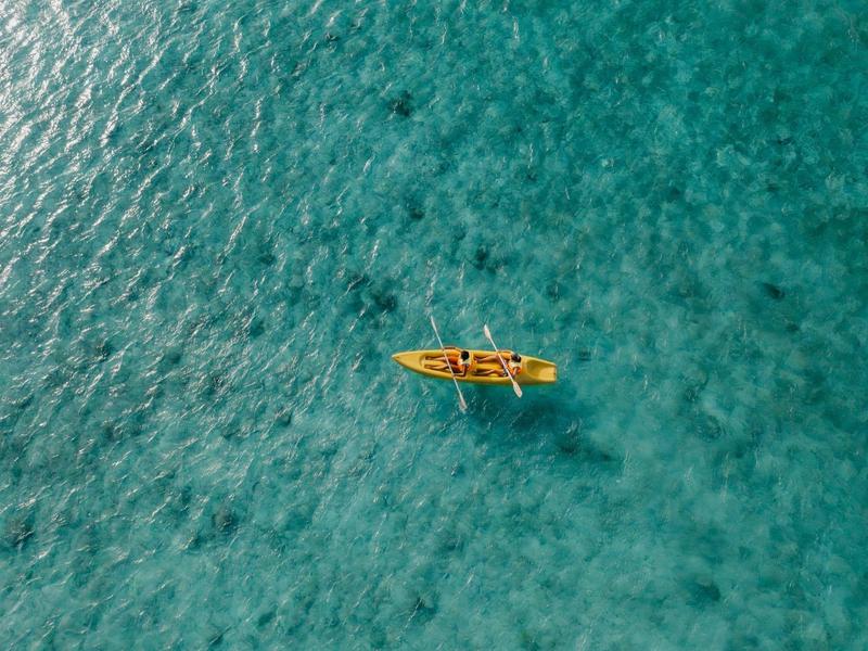 Un kayak jaune sur une eau claire et turquoise, photographié vue de dessus.