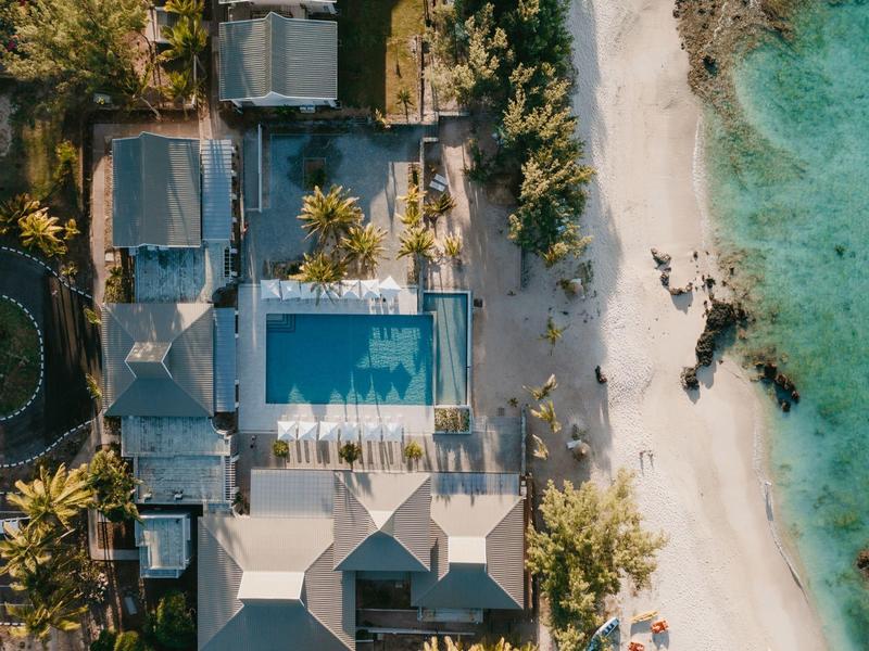 Vue aérienne d'un hôtel avec piscine et accès direct à une plage de sable blanc et eau claire.