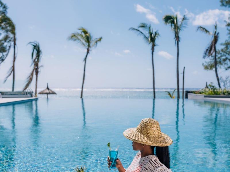 Femme avec chapeau de paille se détend au bord de la piscine avec vue sur les palmiers et la mer.
