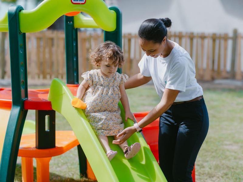 Une femme aide une petite fille à glisser sur un toboggan dans une aire de jeux.