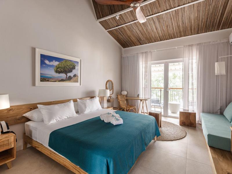 Chambre d'hôtel lumineuse avec lit double, meubles en bois et balcon avec vue sur la verdure.