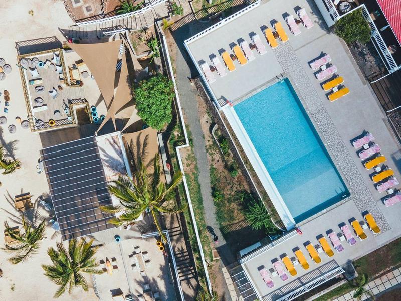 Dakterras met zwembad en ligstoelen naast een wit zandstrand met palmbomen.
