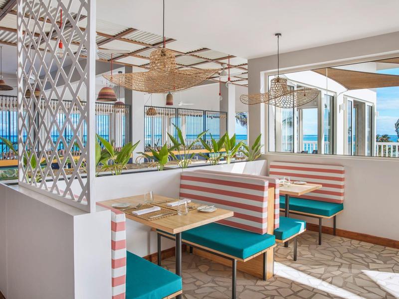 Lichte eetzaal met turquoise banken en uitzicht op zee door grote ramen.