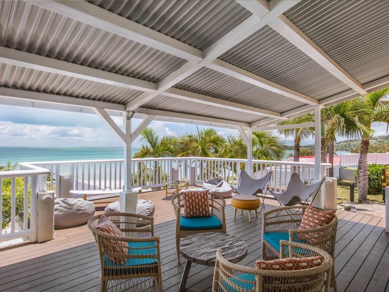 Overdekt terras met kleurrijke stoelen en uitzicht op de oceaan, omringd door palmbomen.