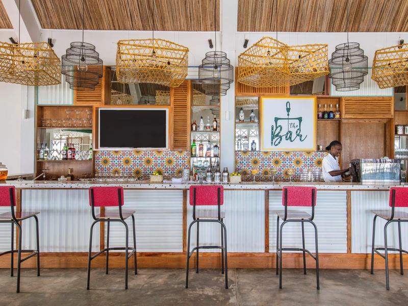 Open bar met krukken met rode zittingen en hanglampen van gevlochten manden in een hotel.