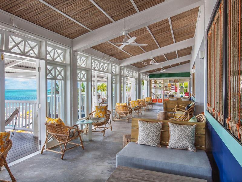 Lichte veranda met rotanmeubilair, uitzicht op zee en houten plafond met ventilatoren.