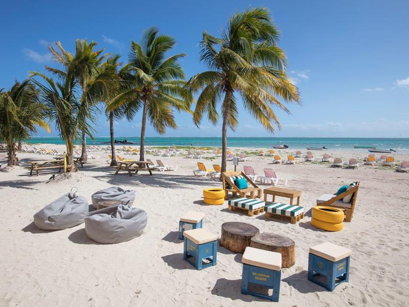 Strand met palmbomen, zitplaatsen en uitzicht op zee bij heldere lucht.