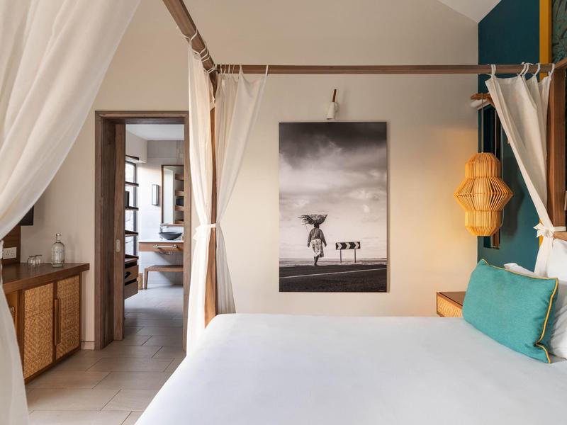 Moderně zařízená ložnice s baldachýnovou postelí, uměleckým obrazem na stěně a přístupem do sousední místnosti.