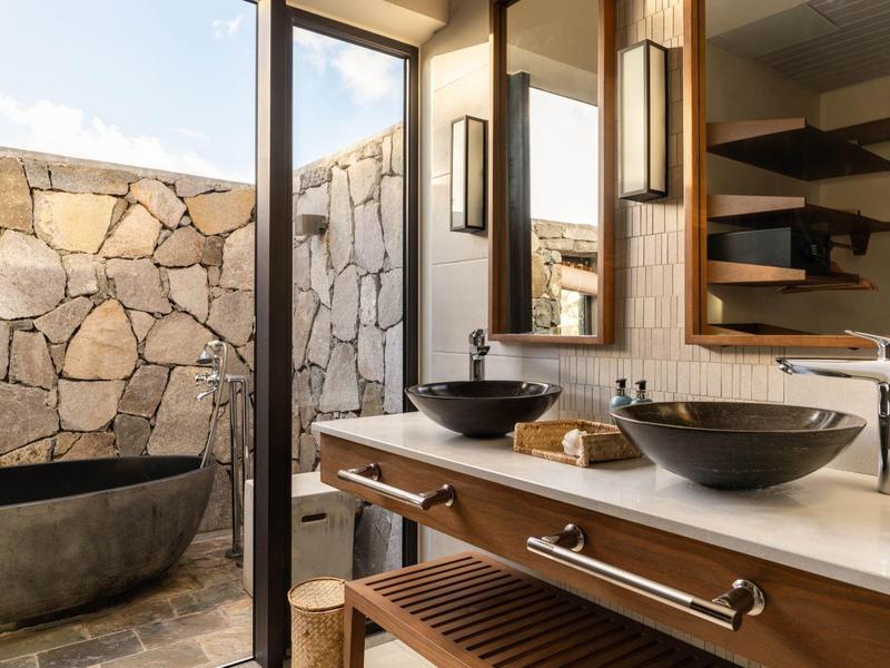 Moderní koupelna s dvojnásobnými černými umyvadly a venkovní vanou se zdí z kamenů.