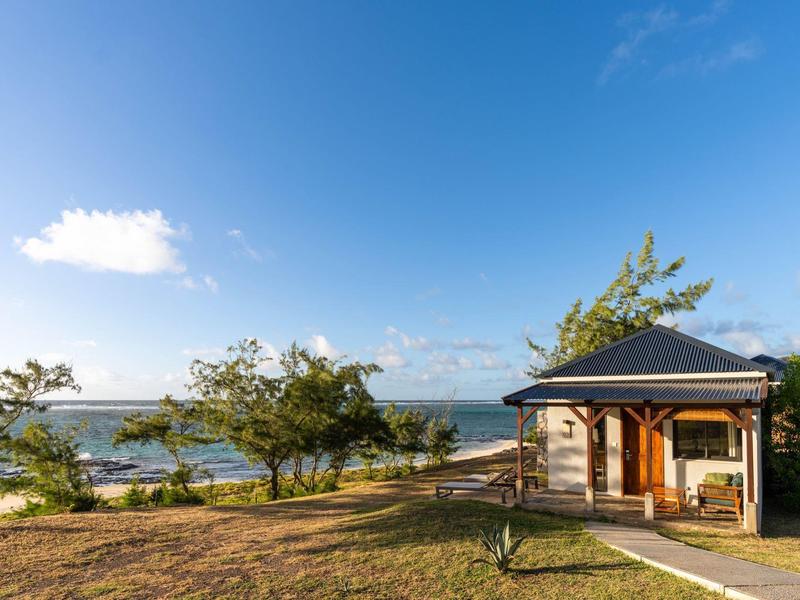 Malý plážový dům s verandou vedle stromů a moře pod modrou oblohou.