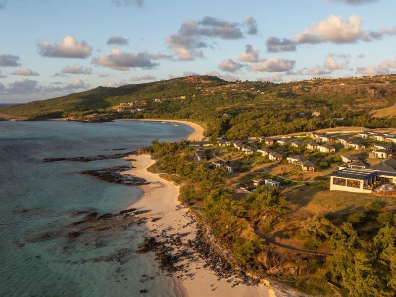 Letecký pohled na pobřežní město s písčitými plážemi, čistou vodou a kopcovitou krajinou za západu slunce.