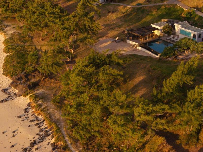 Letecký pohled na dům s bazénem v zalesněné oblasti poblíž písečné pláže.