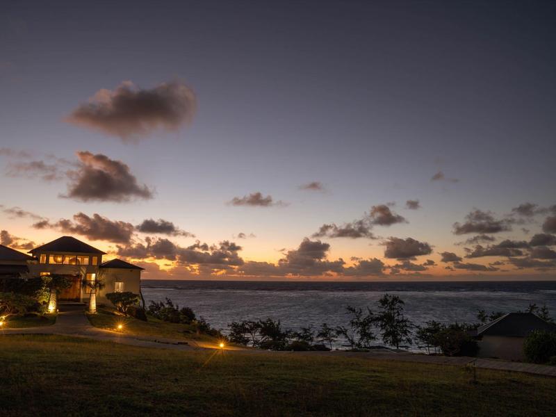 Hotel s osvětlenými venkovními prostory na svahu za soumraku s výhledem na moře.