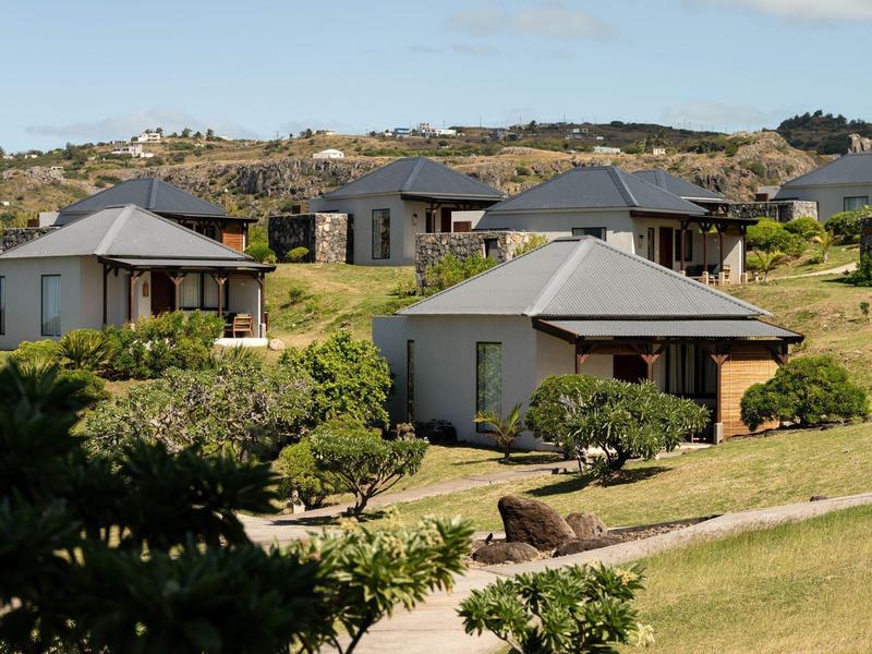Několik malých rekreačních domků v kopcovité krajině s zelenou trávou a keři.