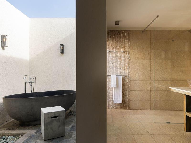 Moderní koupelnový prostor s bezbariérovým sprchovým koutem a volně stojící černou vanou venku.