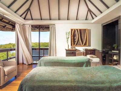 Modern hotel room with two beds, balcony, and view of green landscape.