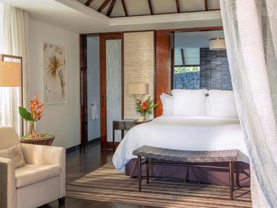 Luxurious hotel room with large bed, armchairs, and natural light.