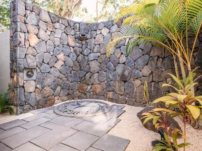 Outdoor shower with natural stone wall and plants in a paved hotel area.