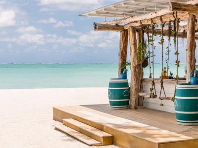 Schaukel unter einer hölzernen Pergola mit Blick auf einen weißen Sandstrand und türkisfarbenes Meer.