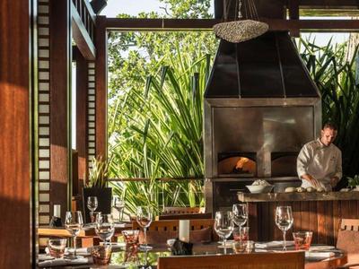 Moderner Restaurantbereich mit Holzmöbeln und Blick auf üppige grüne Pflanzen draußen.