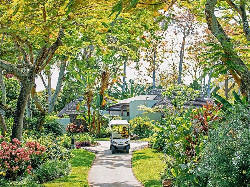 A golf cart drives along a narrow path through a lush, green hotel garden.
