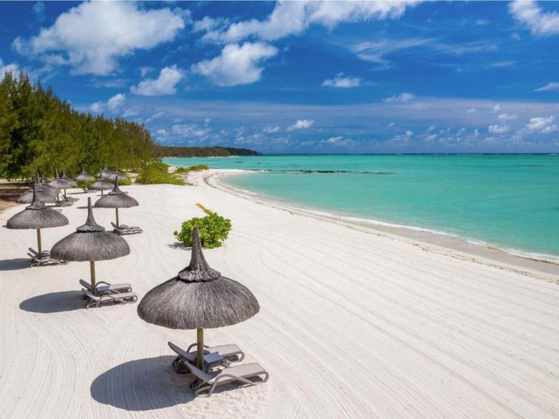 White sandy beach with sun loungers and straw umbrellas by turquoise sea under blue sky.