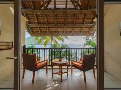Balkon mit zwei Stühlen und einem kleinen Tisch mit Blick auf Palmen und Meer.