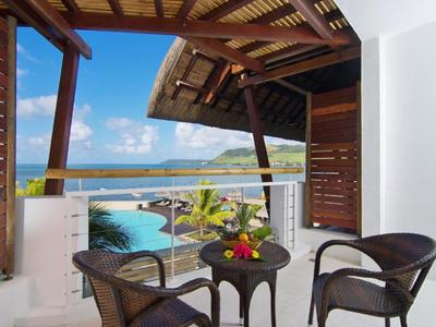 Balkon mit zwei Stühlen und kleinem Tisch mit Blick auf Meer und Pool bei klarem Himmel.