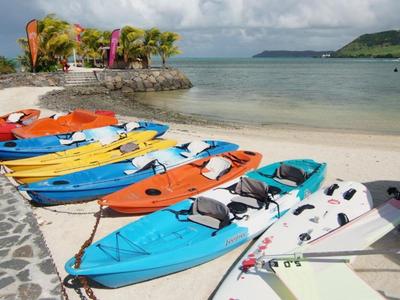 Des kayaks colorés alignés sur une plage de sable avec vue sur une mer calme et des collines vertes.