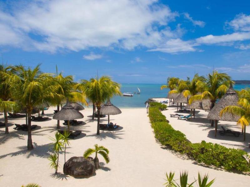 Plage avec palmiers, parasols et sable blanc sous un ciel bleu au bord de la mer.