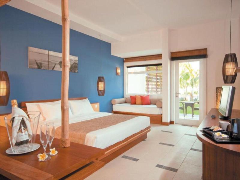 Chambre d'hôtel moderne avec mur bleu, grand lit et coin salon près de la fenêtre.