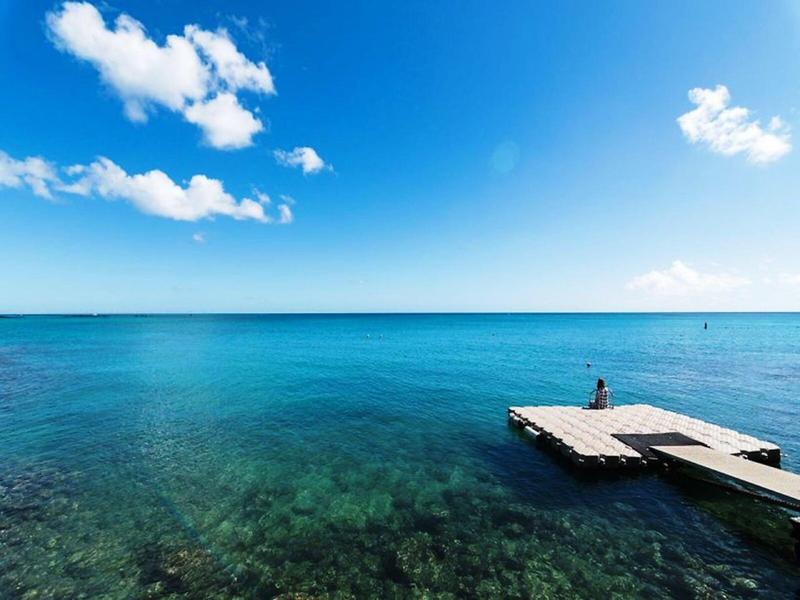 Clear blue sea landscape with small pier and person at the end under sunny sky.