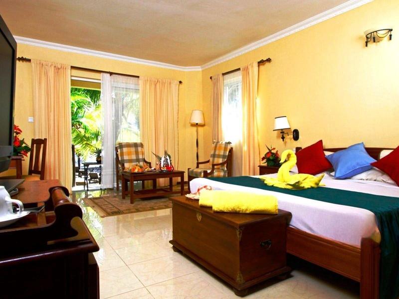 Bright hotel room with double bed, wooden furniture, and balcony overlooking garden.