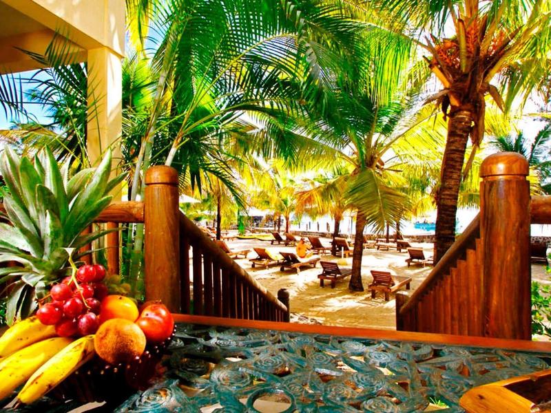 Tropical hotel balcony with exotic fruits and view of palm trees and lounge chairs on the beach.