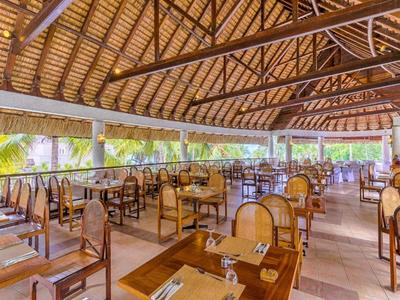 Ampia area ristorante aperta con sedie in legno e vista su piante tropicali.