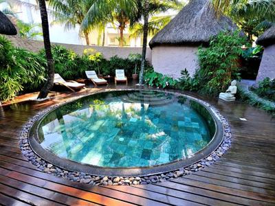 Vasca idromassaggio rotonda con pavimento in legno e sdraio in un giardino tropicale.