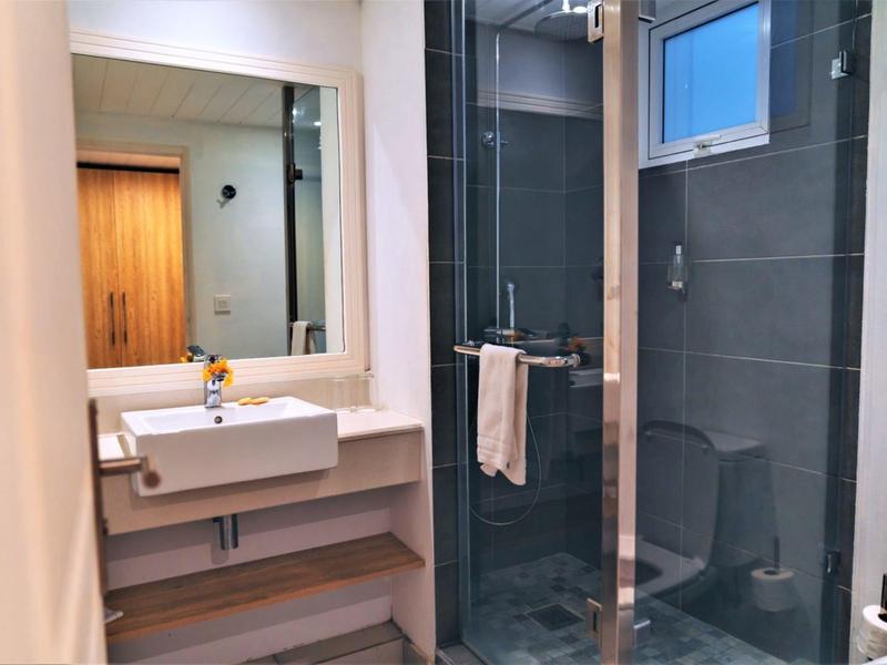 Modernes Badezimmer mit Glasdusche, grauen Fliesen, weißem Waschbecken und großem Spiegel.