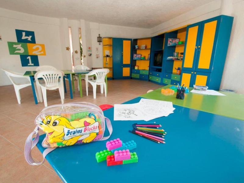 Buntes Klassenzimmer mit buntem Möbel, Spielzeug, Stiften und zwei weißen Tischen mit Stühlen.