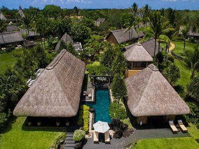 Blick auf tropisches Resort mit Strohdachbungalows, Pool und grünem Palmengarten unter blauem Himmel.