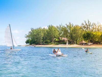 Kleine Segelboote und Kajaks auf blauem Wasser vor einer bewaldeten Insel unter klarem Himmel.
