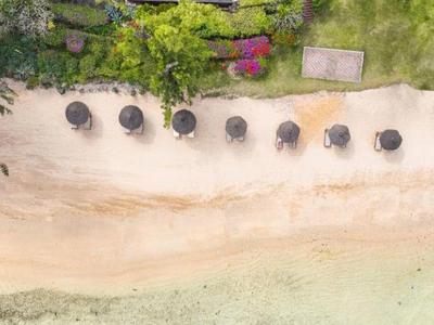 Luftaufnahme eines Strandes mit Sonnenschirmen, klarem Wasser und drei Booten am Ufer.
