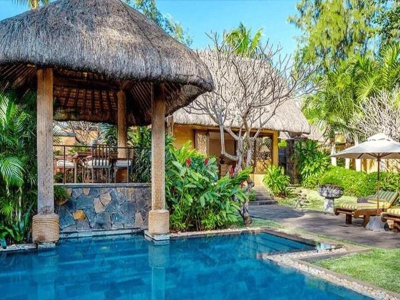 Ein tropischer Poolbereich mit Strohdach, grünen Pflanzen und Liegestühlen an einem sonnigen Tag.