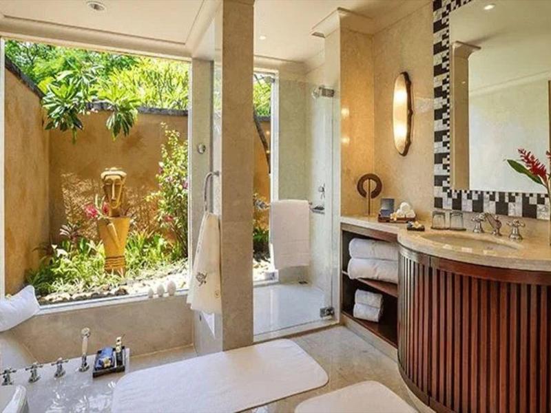 Helles Badezimmer mit großer Badewanne, Balkon, Holzwaschtisch und Pflanzen vor der Tür.