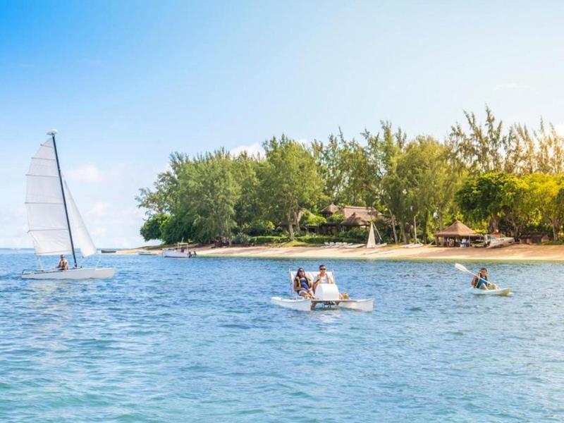 Kleine Segelboote und Kajaks auf blauem Wasser vor einer bewaldeten Insel unter klarem Himmel.