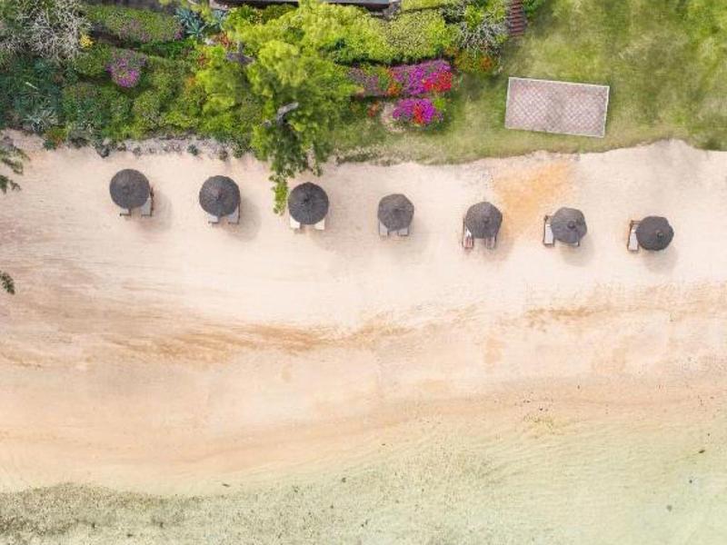 Luftaufnahme eines Strandes mit Sonnenschirmen, klarem Wasser und drei Booten am Ufer.